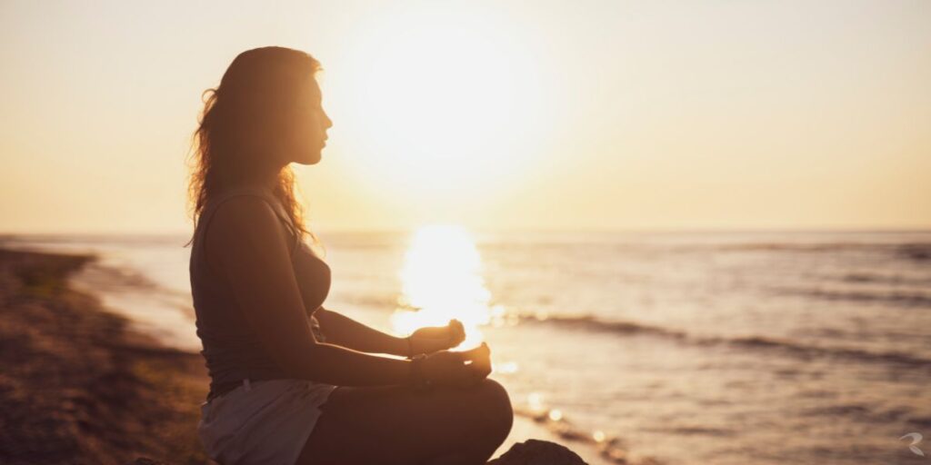 A woman meditating at sunrise, eyes closed in peaceful reflection — symbolising the message of pain and inner healing.