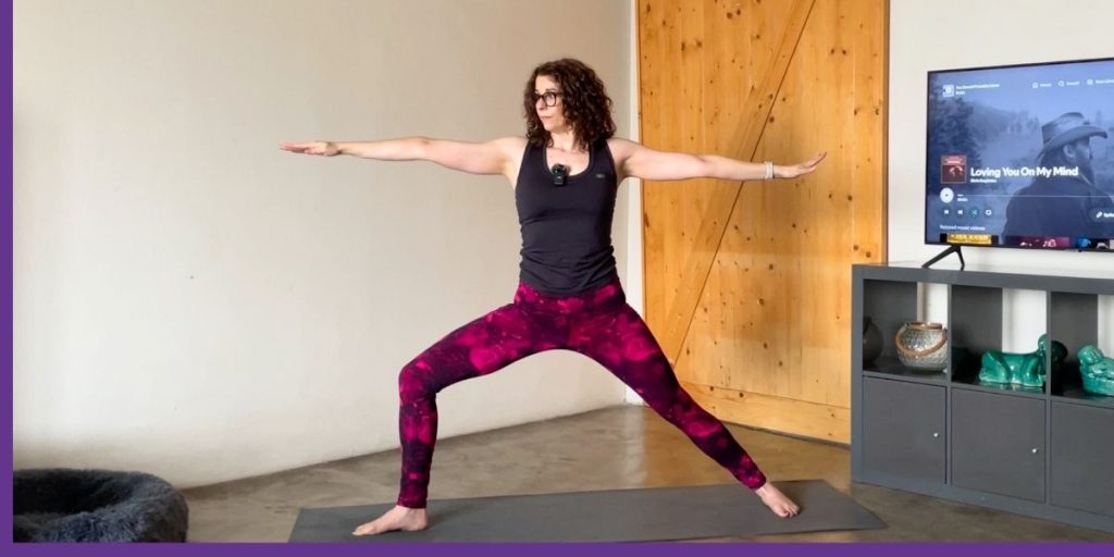 Woman practising Warrior II pose during a modified power yoga routine at home