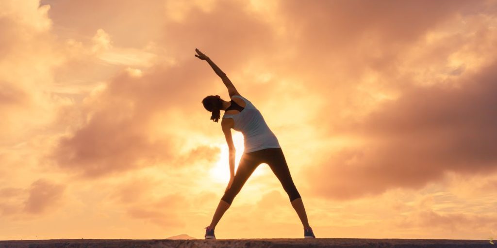 Woman stretching at sunrise, symbolising movement as medicine for body, mind, and spirit