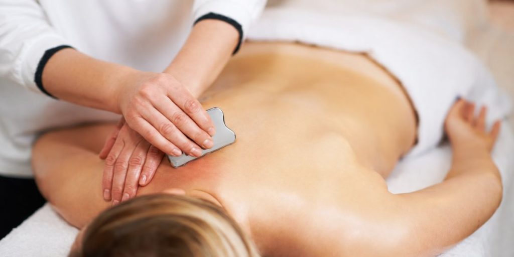 Using a stainless steel Gua Sha tool on upper back muscle tension